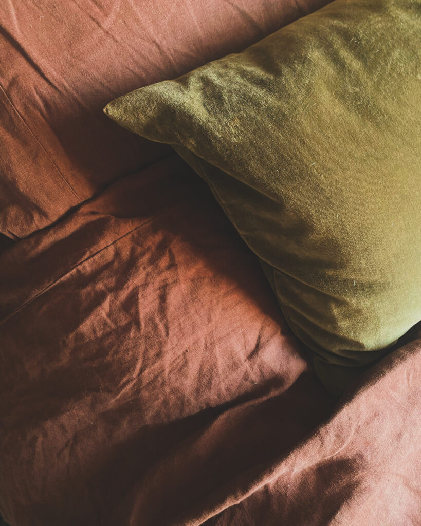 Close up of crisp, linen bedding in a chocolate brown colour decorated with an olive green, velvet cushion