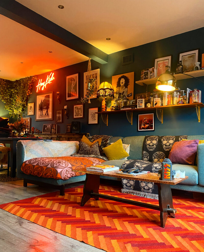 A retro inspired living room primarily using orange and blue as the colour palette. A corner sofa sits against a maximalist backdrop and a neon sign in pink is lit up with the words 'hey kid'. 